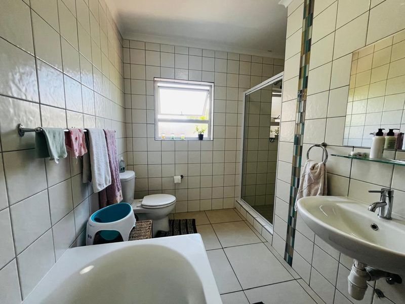 A functional bathroom featuring a shower enclosure, pedestal washbasin, toilet, and neutral ceramic tiling throughout.