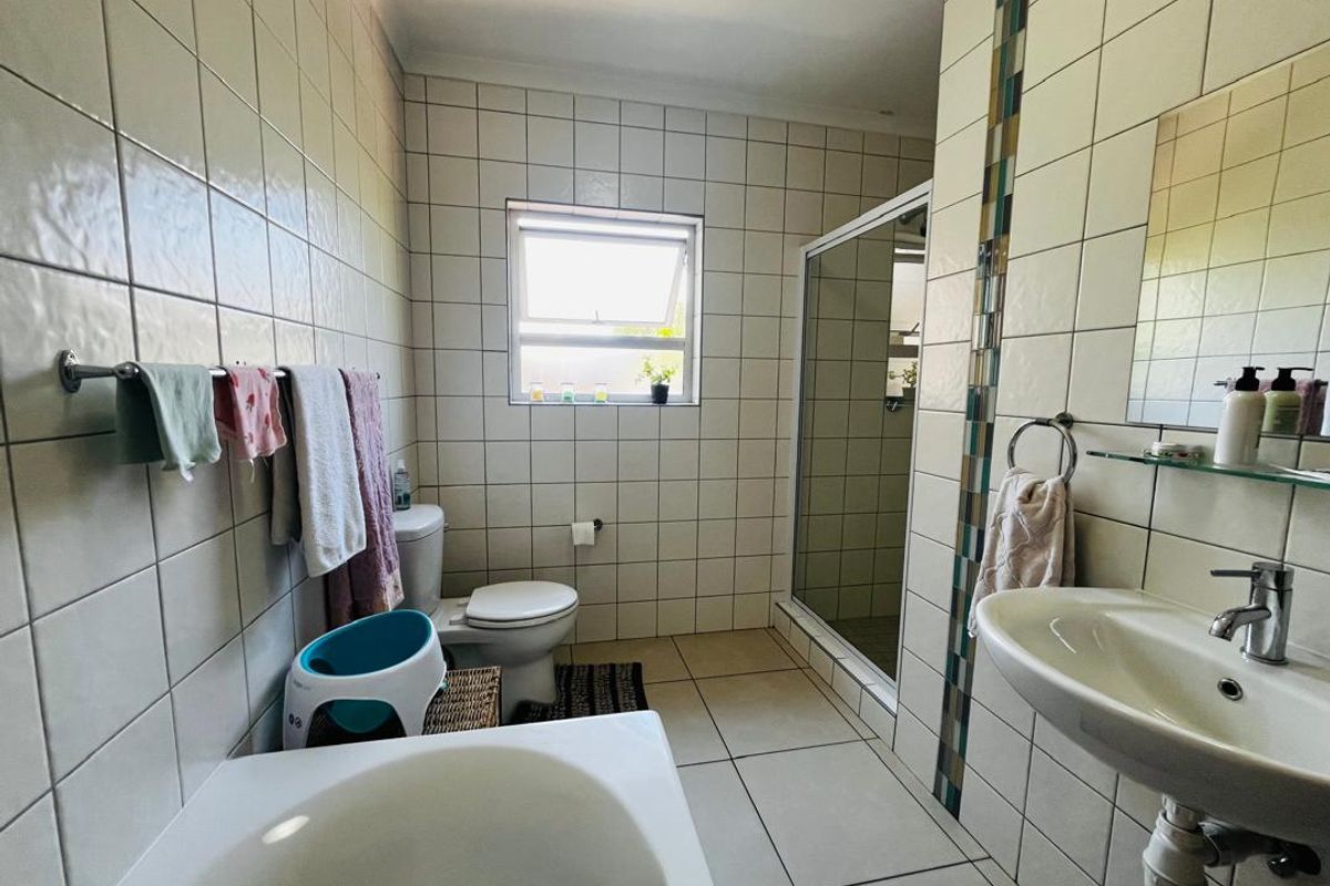 A functional bathroom featuring a shower enclosure, pedestal washbasin, toilet, and neutral ceramic tiling throughout.