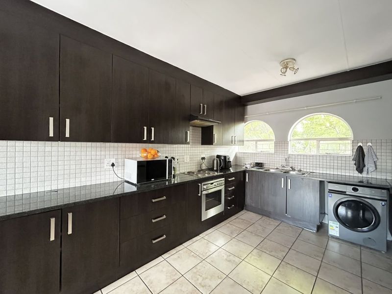 Functional kitchen featuring dark wood cabinetry, granite countertops, tiled backsplash, built-in oven, and integrated laundry appliance space with arched windows.