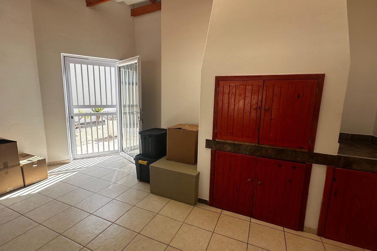 An interior living space featuring tiled flooring, a built-in fireplace with red wooden cabinetry, and a security door leading to the exterior.