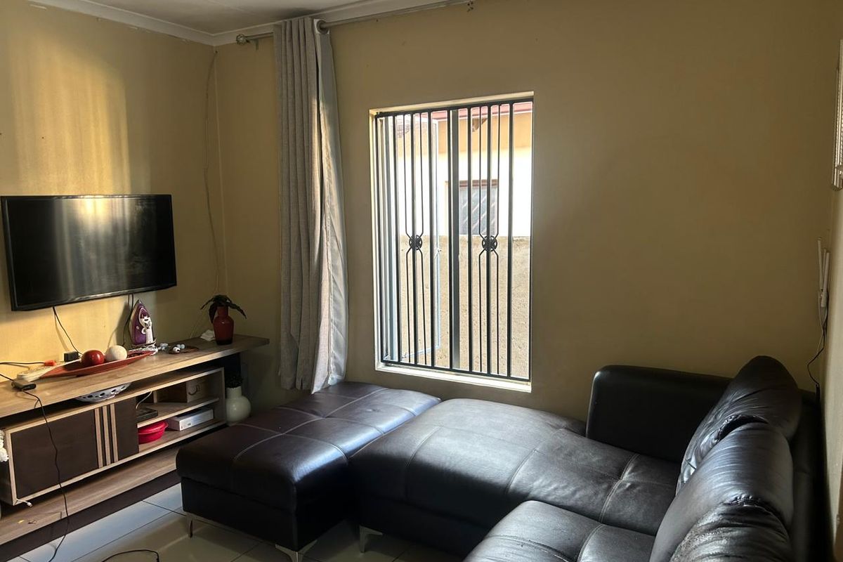 A cozy living room featuring tiled flooring, a window with security bars, and neutral wall tones, providing a functional and comfortable living space.