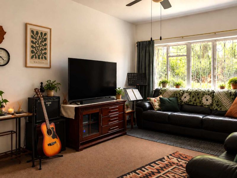 A cozy living room featuring a large window with security bars, a ceiling fan, and neutral wall finishes.