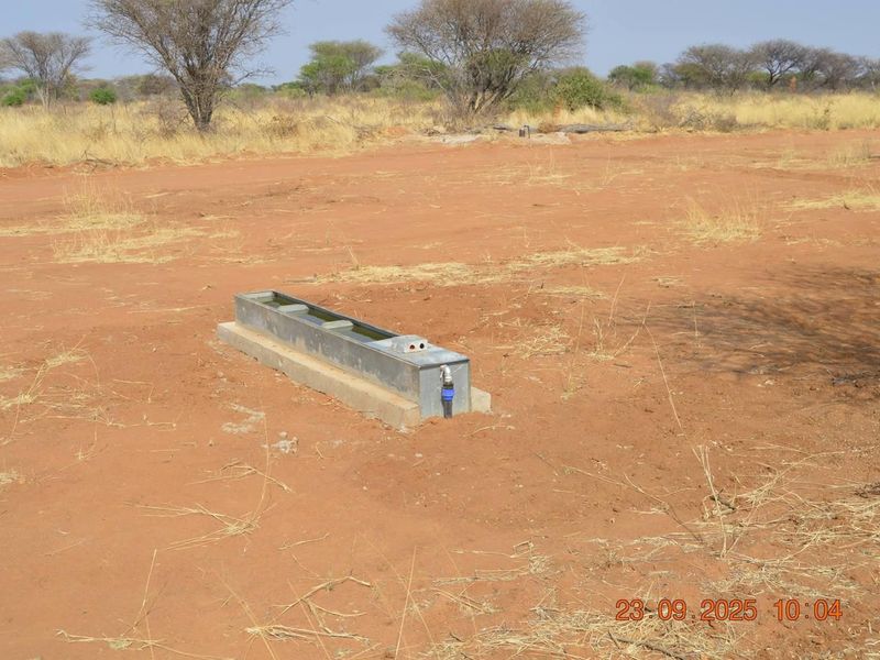 An open agricultural field featuring a fixed metal livestock water trough with connected water supply infrastructure.