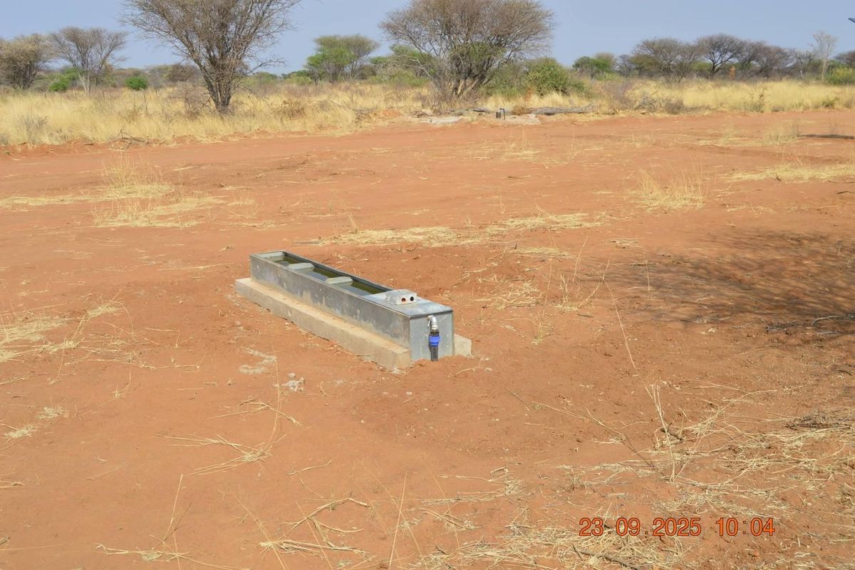 An open agricultural field featuring a fixed metal livestock water trough with connected water supply infrastructure.