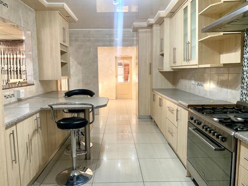 A well-maintained kitchen featuring light wood cabinetry, granite-look laminate countertops, a gas stove with extractor fan, and polished floor tiles.