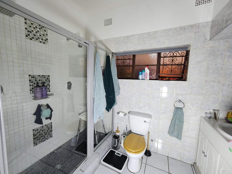 A functional bathroom featuring a glass-enclosed shower, tiled walls, and a built-in vanity cabinet, offering potential for modernization and cosmetic updates.