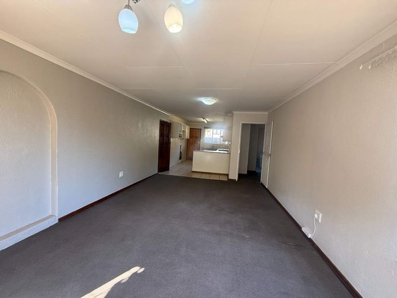 An open-plan living and kitchen area featuring carpeted flooring in the living space, tiled kitchen floors, and built-in cabinetry.
