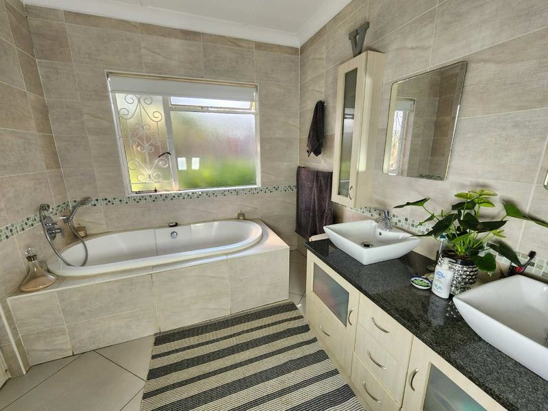 A well-maintained bathroom featuring a built-in bathtub, double vanity with vessel sinks, granite countertops, and neutral wall tiling.
