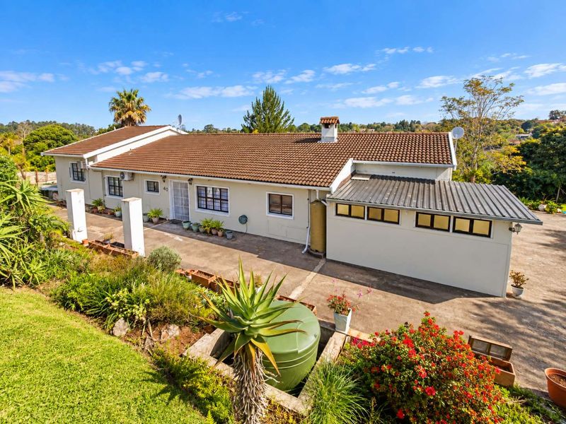 A rear view of the house featuring a tiled roof, concrete driveway, and a water tank, set within a landscaped garden area.
