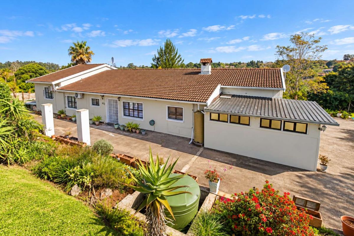 A rear view of the house featuring a tiled roof, concrete driveway, and a water tank, set within a landscaped garden area.