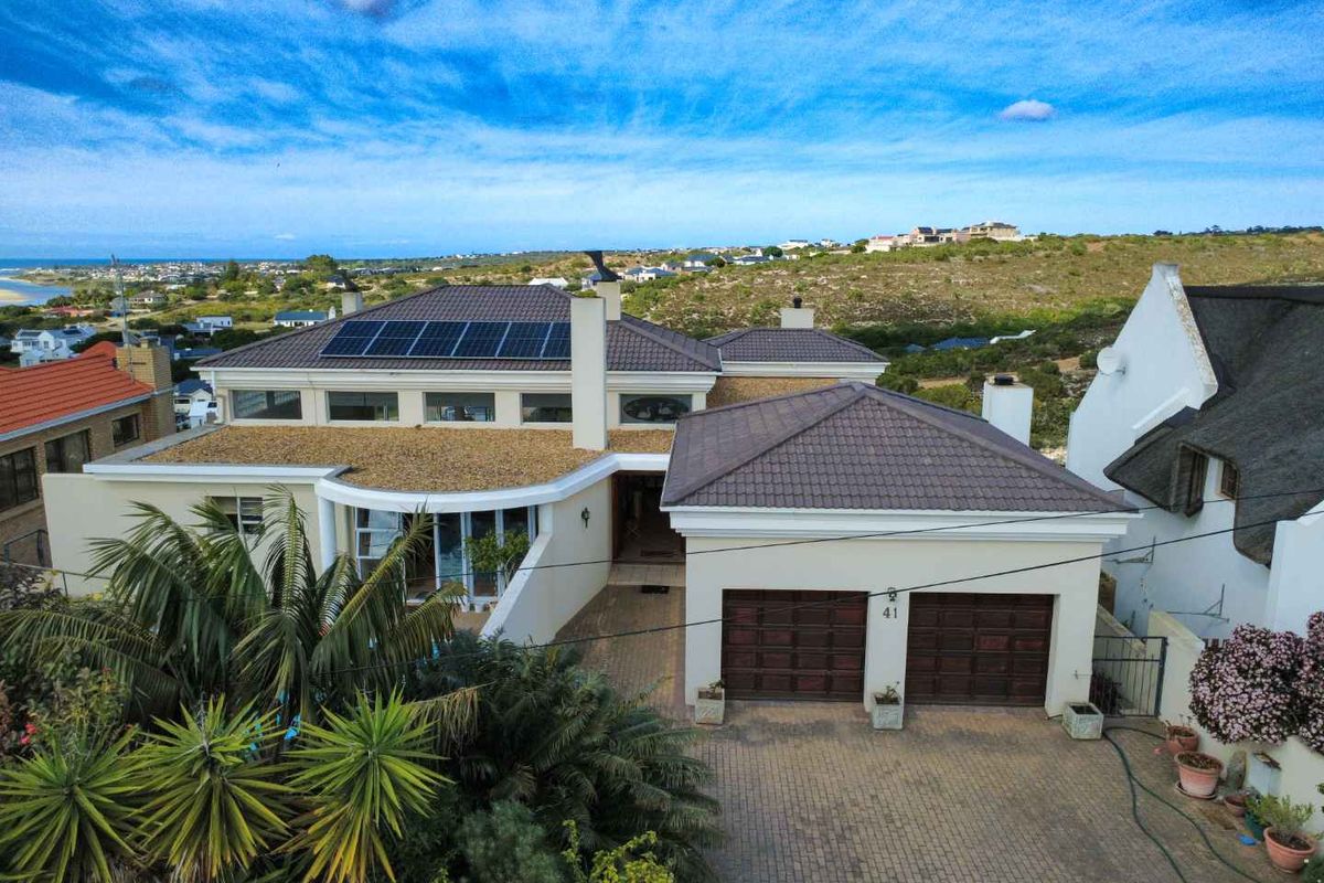 Aerial view of a modern residential property featuring a tiled roof, integrated solar panels, double garage, and paved driveway in a coastal setting.