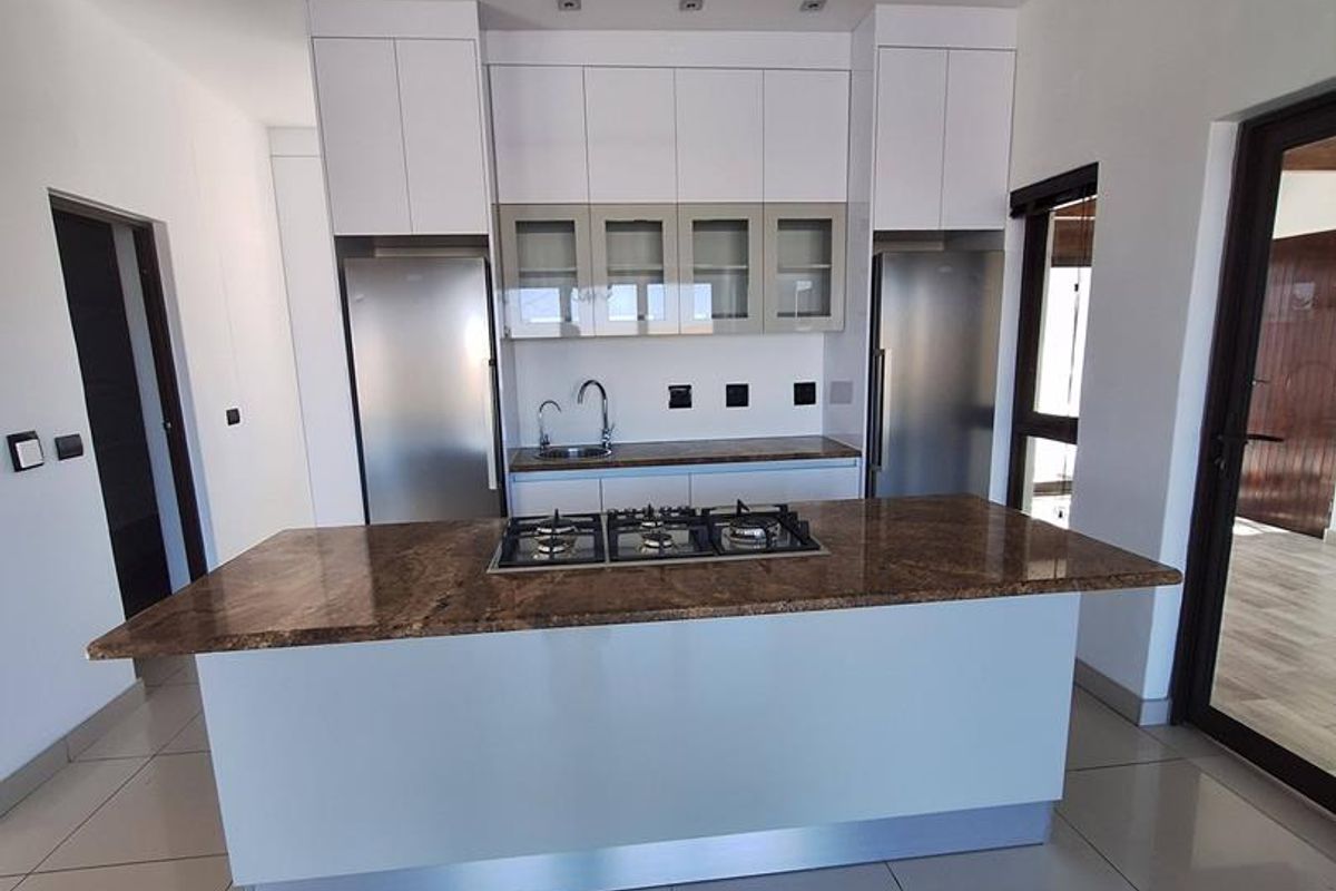 Modern kitchen featuring a central island with a built-in gas hob, granite countertops, sleek white cabinetry, and large format floor tiles.