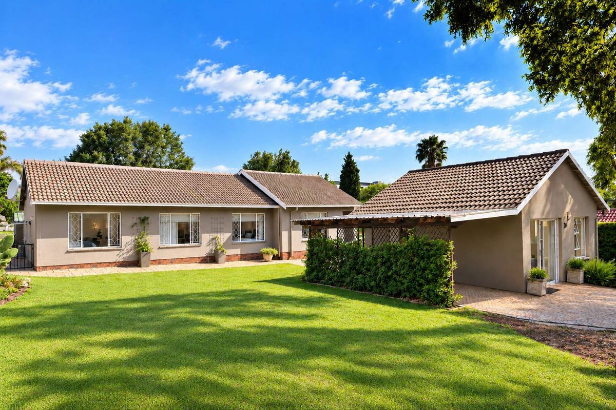 A well-maintained rear exterior view of the house featuring a spacious lawn, paved patio area, and a covered pergola structure.