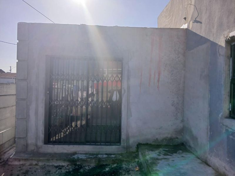 Rear exterior view showing a sliding door with a security gate and concrete step, featuring unfinished wall surfaces and visible staining.
