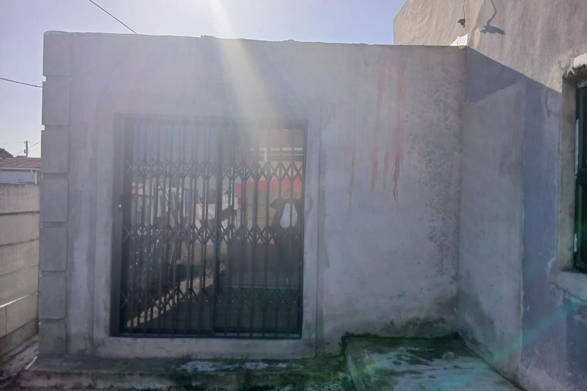 Rear exterior view showing a sliding door with a security gate and concrete step, featuring unfinished wall surfaces and visible staining.