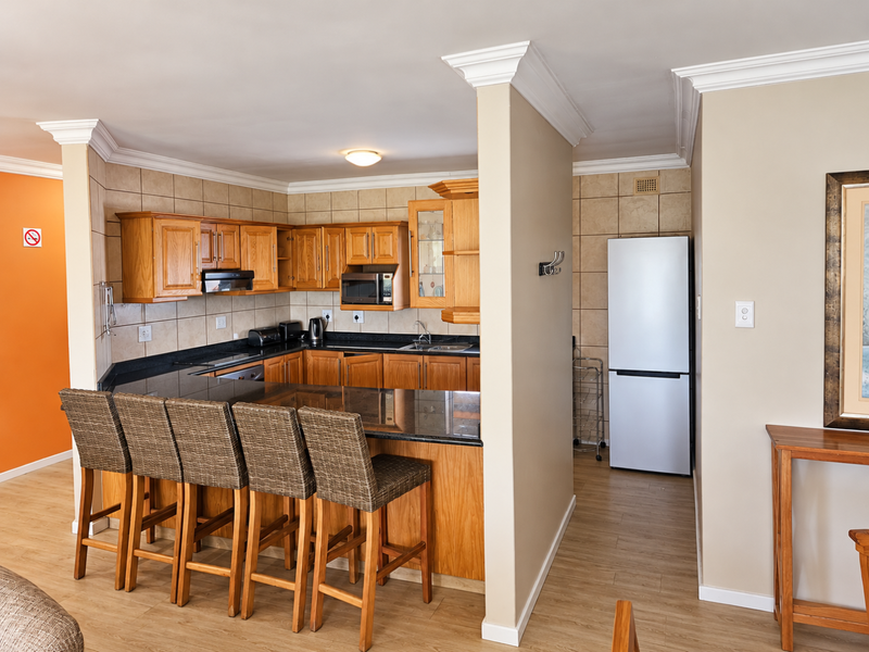 Open plan kitchen featuring wooden cabinetry, granite countertops, and a breakfast bar, seamlessly integrated with the living area.