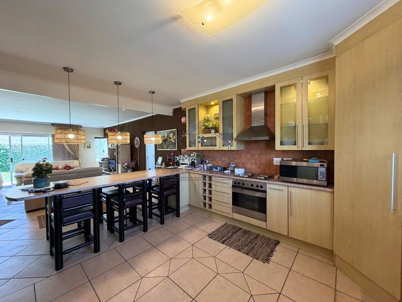 Open plan kitchen and living area featuring light wood cabinetry, tiled flooring, and a breakfast bar, creating a functional and connected living space.