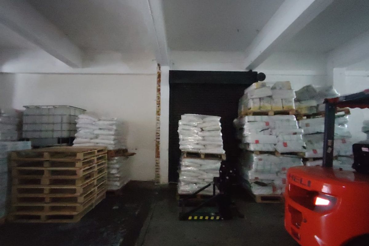 Industrial warehouse storage area featuring exposed concrete beams, a roller shutter door, and concrete flooring, currently utilized for palletized goods storage.