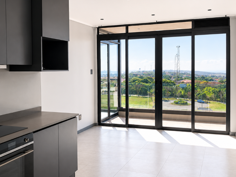 Modern open-plan kitchen featuring sleek dark cabinetry, integrated appliances, and large sliding doors opening to a balcony with expansive views.