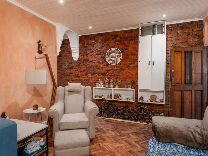 Cozy living room featuring a rustic exposed brick wall, classic herringbone parquet flooring, and built-in storage cabinetry with recessed ceiling lighting.