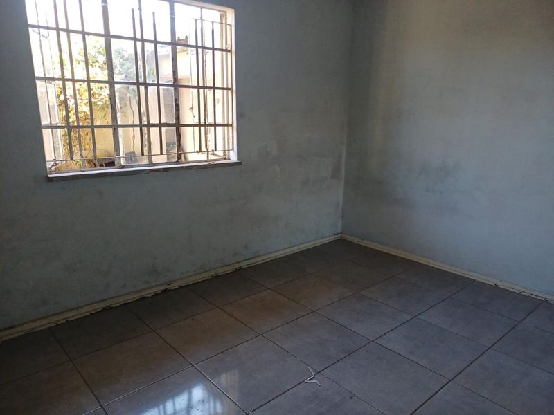 An empty bedroom featuring tiled flooring and security bars on the window, requiring cosmetic updates to the walls and finishes.