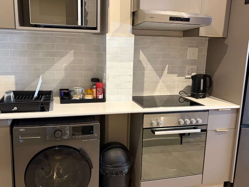 Modern kitchen featuring sleek cabinetry, quartz countertops, subway tile backsplash, and integrated appliances including an oven, hob, extractor fan, and microwave.
