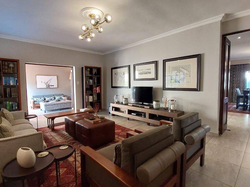 Spacious living room featuring tiled flooring, coved cornicing, and a decorative ceiling rose with modern lighting, offering an open flow to adjacent living areas.