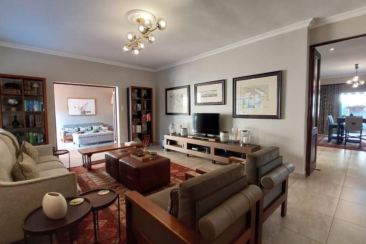 Spacious living room featuring tiled flooring, coved cornicing, and a decorative ceiling rose with modern lighting, offering an open flow to adjacent living areas.