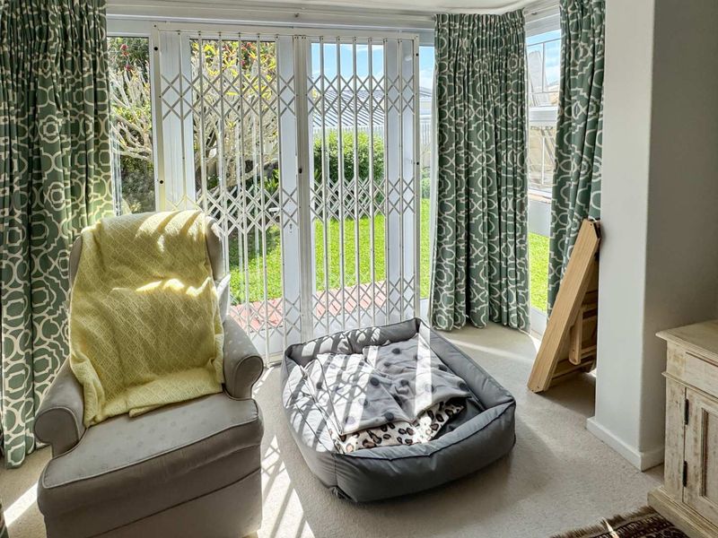 A bright living area featuring large sliding glass doors with security gates, providing direct access to the garden and ample natural light.