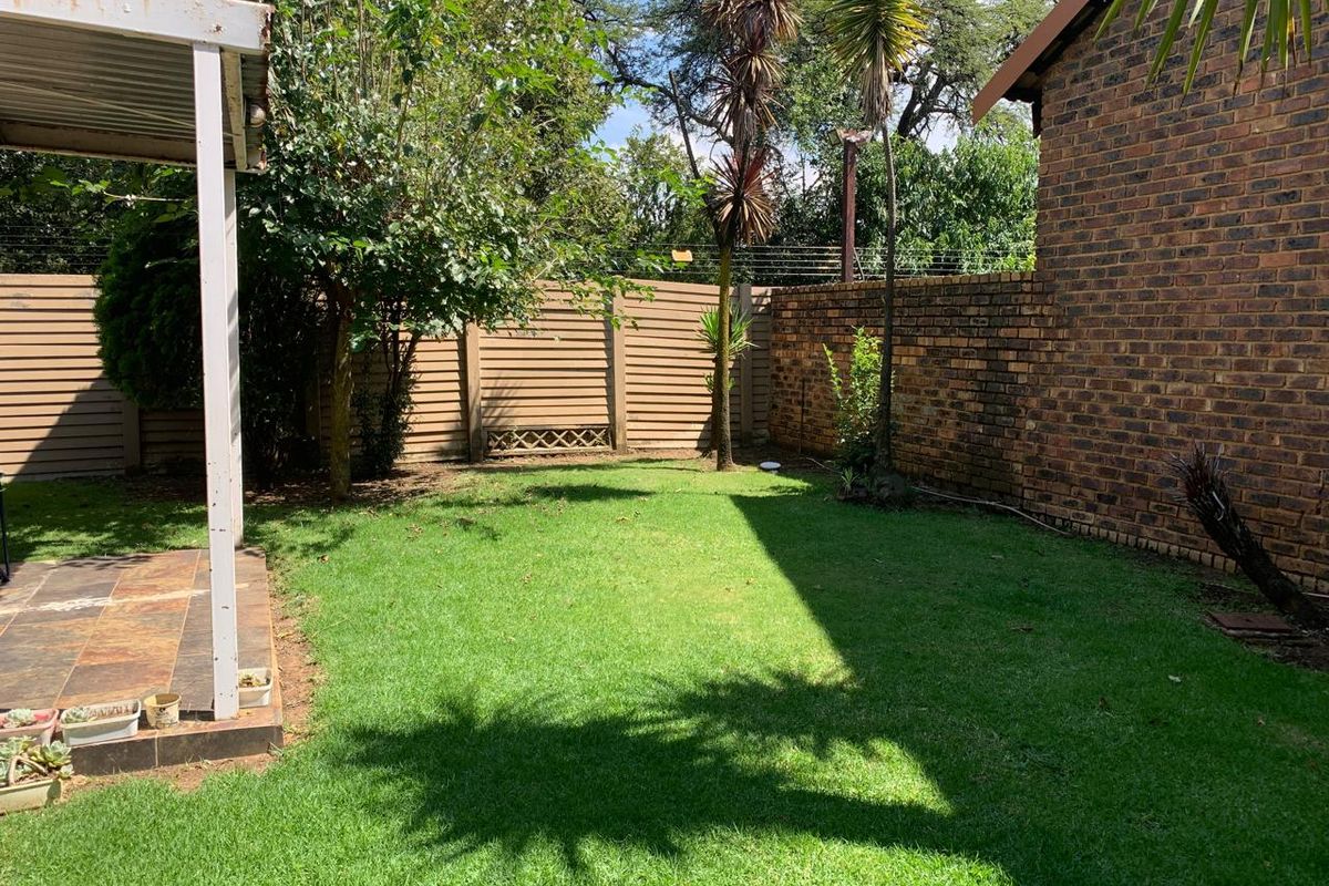 A private rear garden featuring a small tiled patio area, established lawn, and a combination of brick and panel boundary walls.
