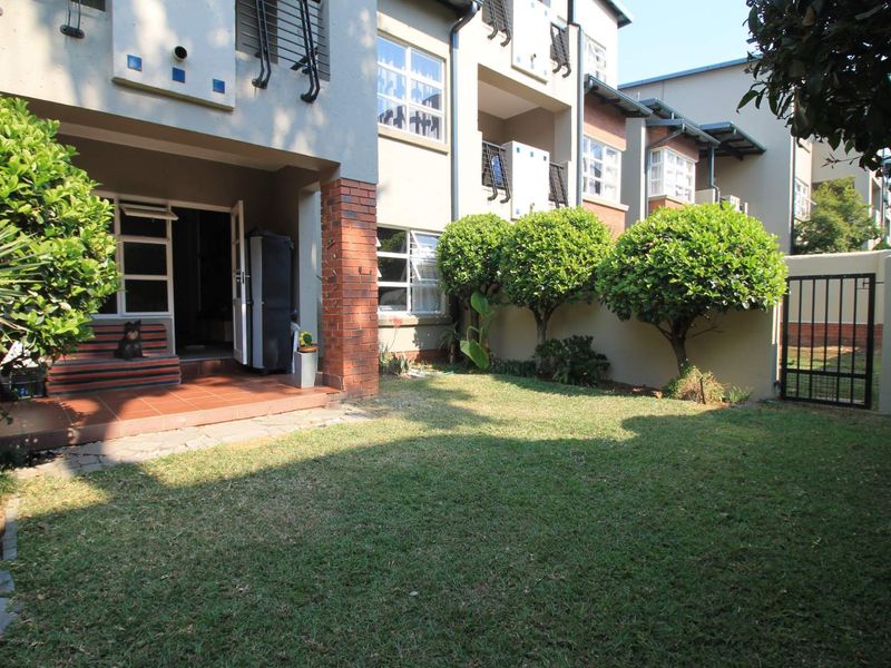 A private rear garden featuring a tiled patio area, established lawn, and secure boundary wall with a metal gate.