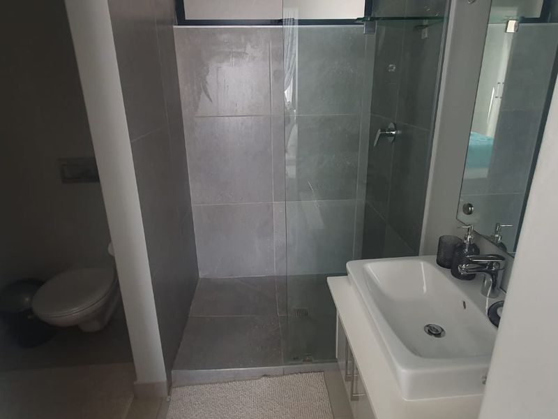 A modern bathroom featuring a glass-enclosed shower, vanity basin with mixer tap, and a separate toilet area with neutral tiling.