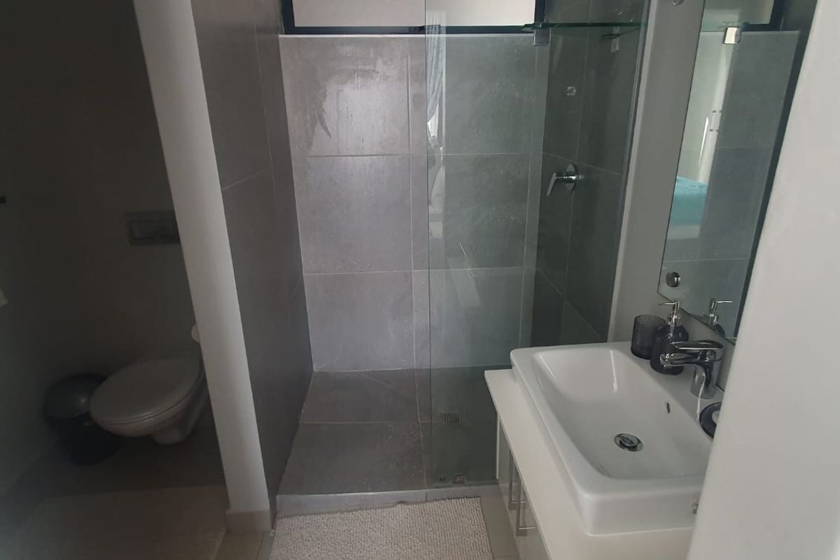 A modern bathroom featuring a glass-enclosed shower, vanity basin with mixer tap, and a separate toilet area with neutral tiling.