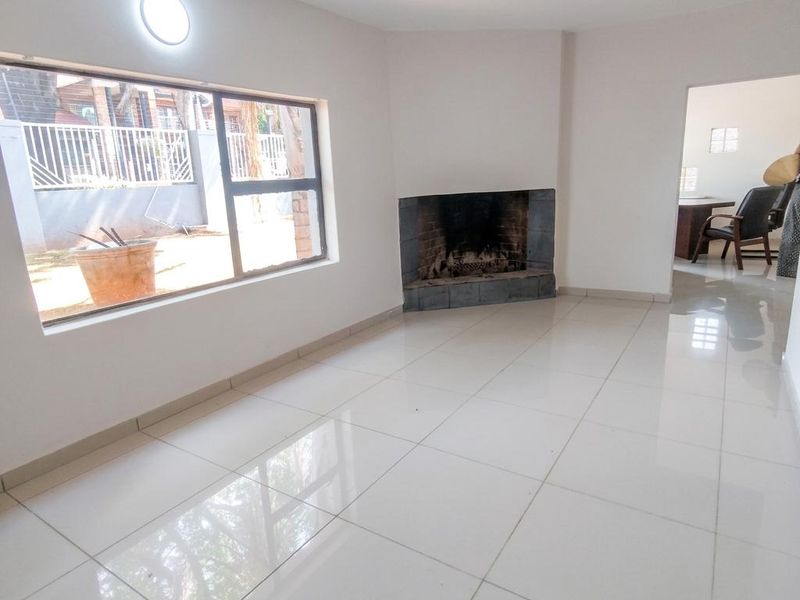 A bright, empty living room featuring large windows, polished tile flooring, and a built-in corner fireplace, offering a clean and neutral space.