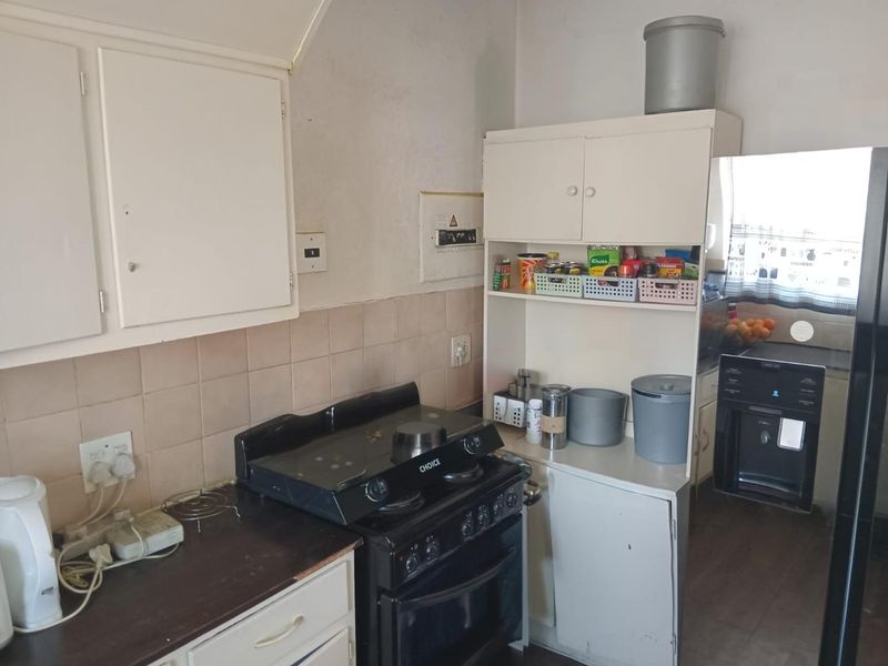 A functional kitchen featuring built-in cabinetry, a tiled backsplash, and a freestanding stove, currently showing signs of wear and dated finishes.