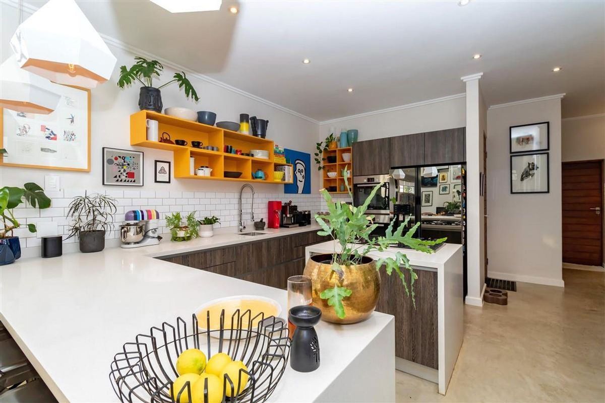 Modern kitchen featuring sleek dark wood cabinetry, white stone countertops, subway tile backsplash, and a functional island with integrated cooktop.