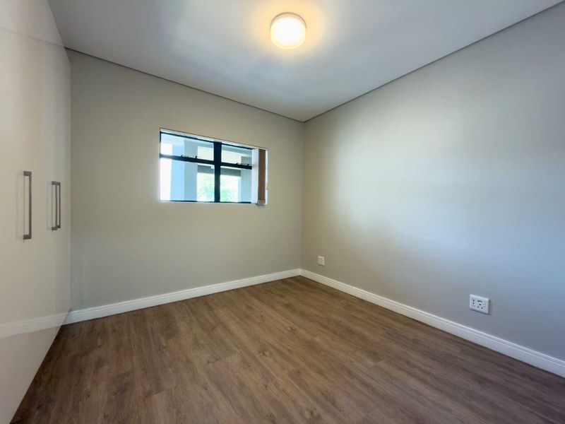 A clean, empty bedroom featuring modern laminate flooring, neutral wall paint, and built-in cupboards, offering a versatile space ready for personalization.