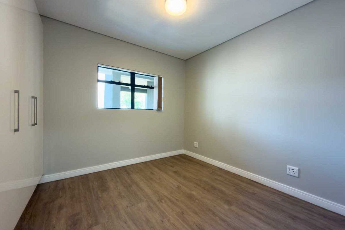A clean, empty bedroom featuring modern laminate flooring, neutral wall paint, and built-in cupboards, offering a versatile space ready for personalization.