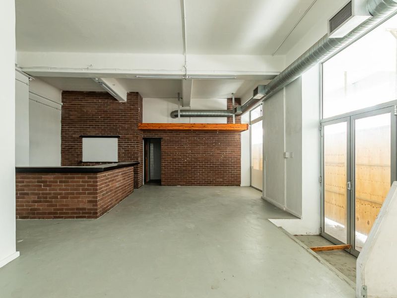 Spacious open-plan area featuring industrial-style exposed brick walls, exposed ducting, and a built-in brick bar counter, offering a versatile layout for various commercial uses.