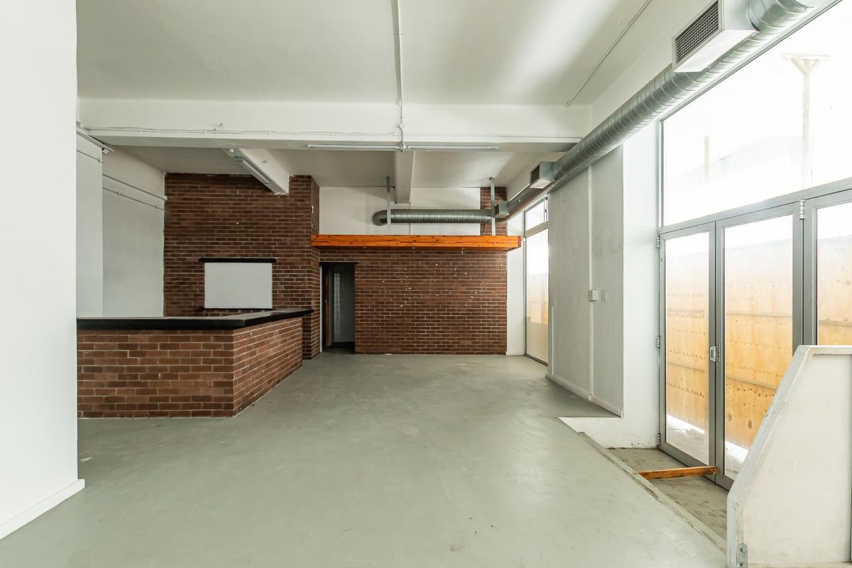 Spacious open-plan area featuring industrial-style exposed brick walls, exposed ducting, and a built-in brick bar counter, offering a versatile layout for various commercial uses.