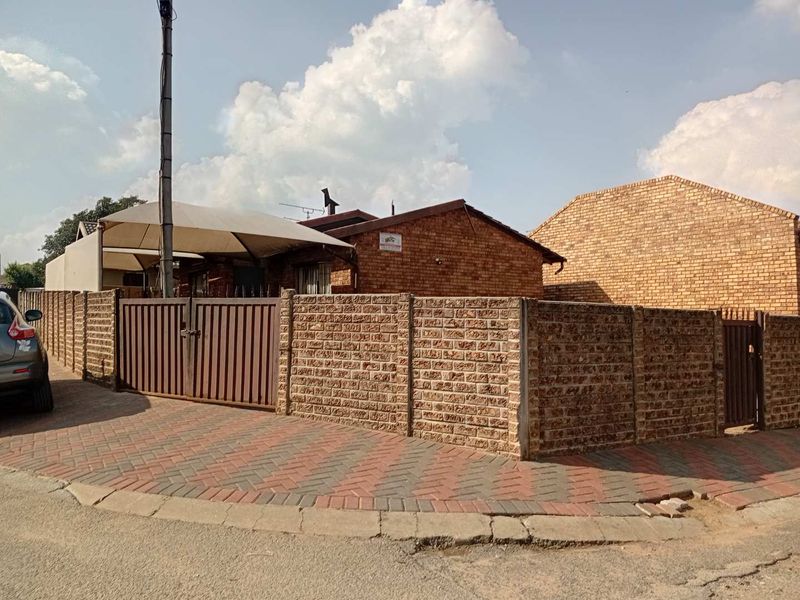 Front exterior view of a face brick house featuring a paved driveway, secure metal gate, and a shade sail over the entrance area.