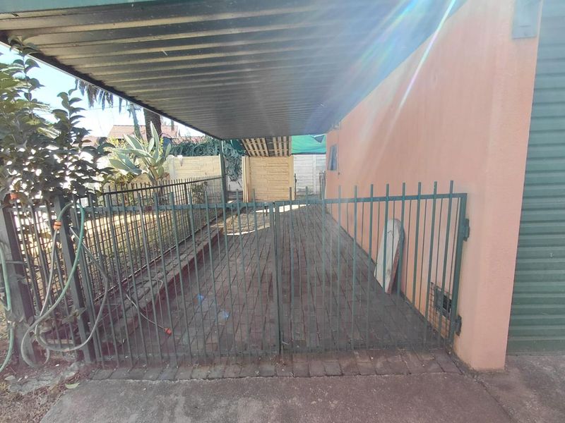 A covered carport area featuring a paved driveway and secure metal gate access, providing sheltered off-street parking.