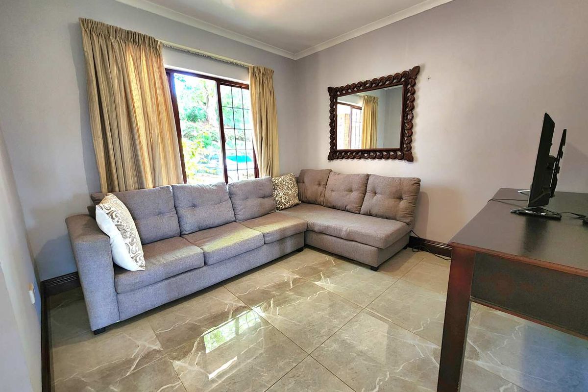 A living room featuring large format polished floor tiles, a window with garden views, and neutral wall finishes.