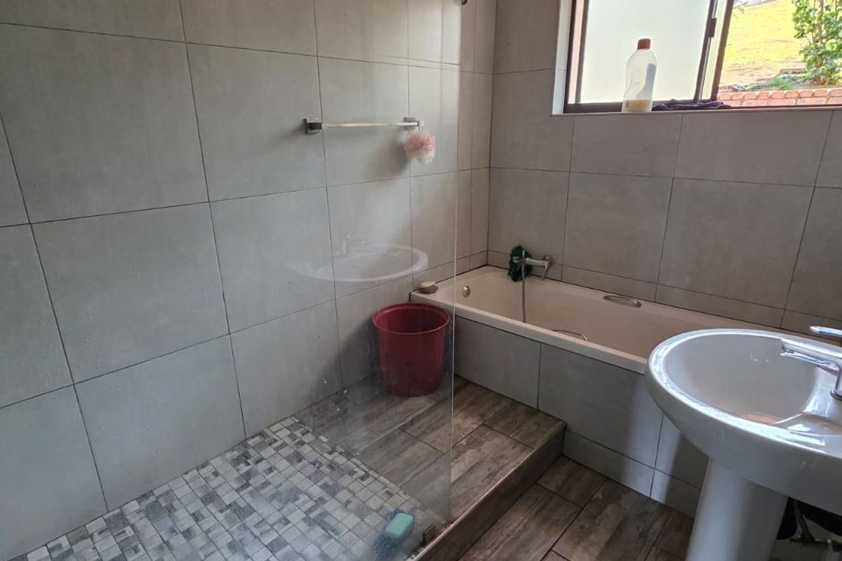 A functional bathroom featuring a tiled shower area with glass screen, a built-in bathtub, and a pedestal basin with modern mixer taps.