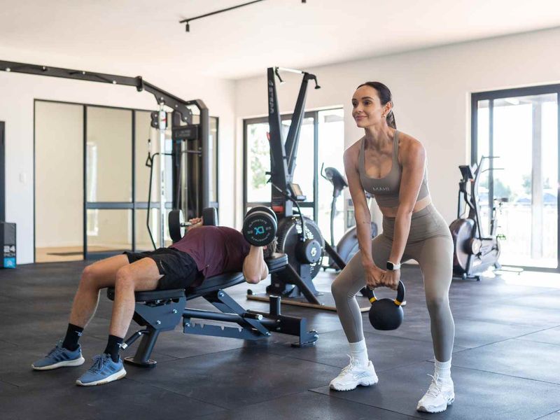 A modern, well-lit home gym featuring rubber flooring, large glass sliding doors, and ample space for fitness equipment.