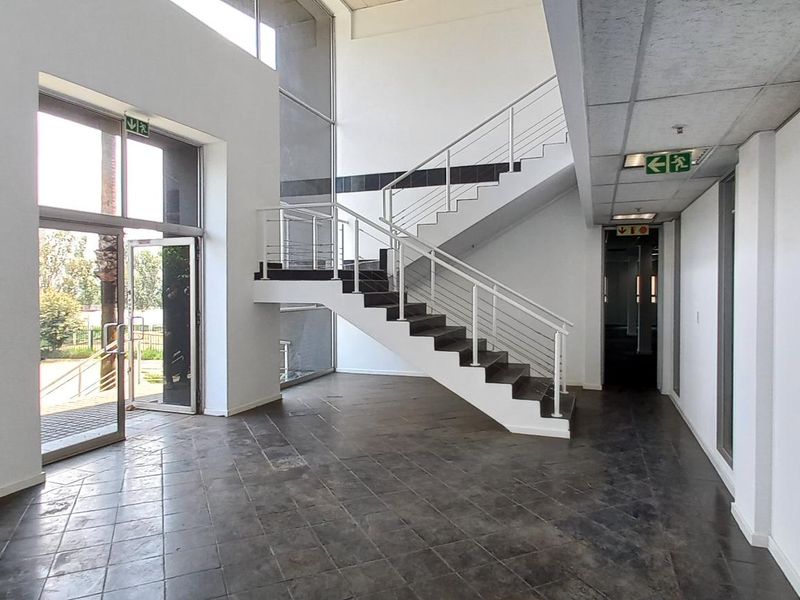 Spacious industrial entrance foyer featuring a central staircase, large glass windows for natural light, and durable tiled flooring.