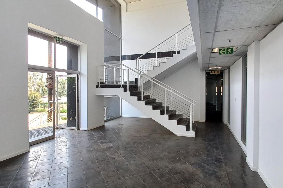 Spacious industrial entrance foyer featuring a central staircase, large glass windows for natural light, and durable tiled flooring.