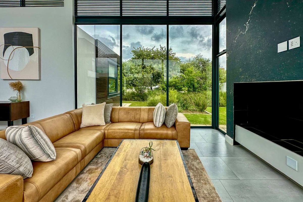 Modern living room featuring expansive floor-to-ceiling windows, sleek tiled flooring, and a striking dark feature wall with integrated media storage.