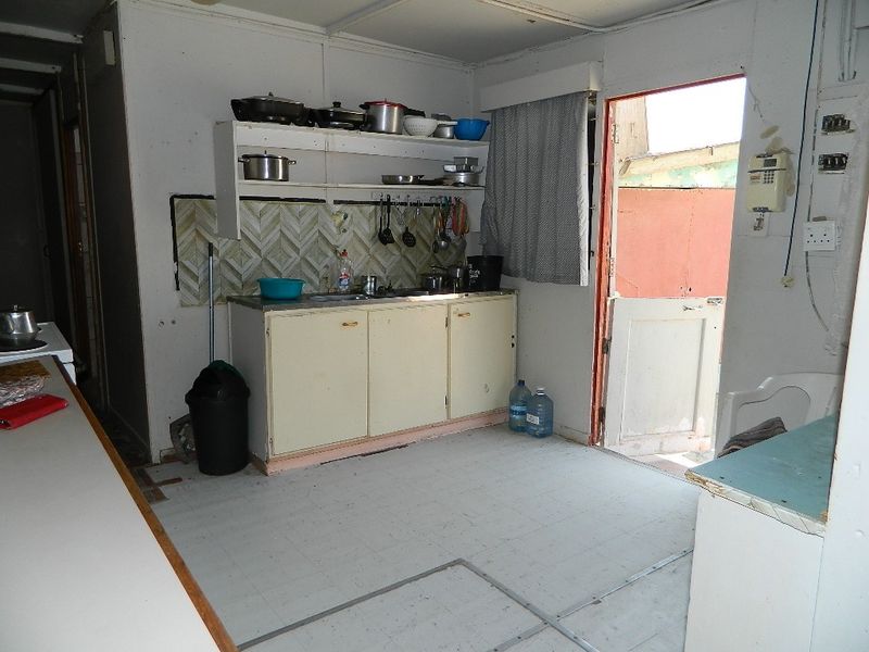 A dated kitchen area featuring basic cabinetry, open shelving, and a tiled backsplash, requiring significant renovation to modernize the space.