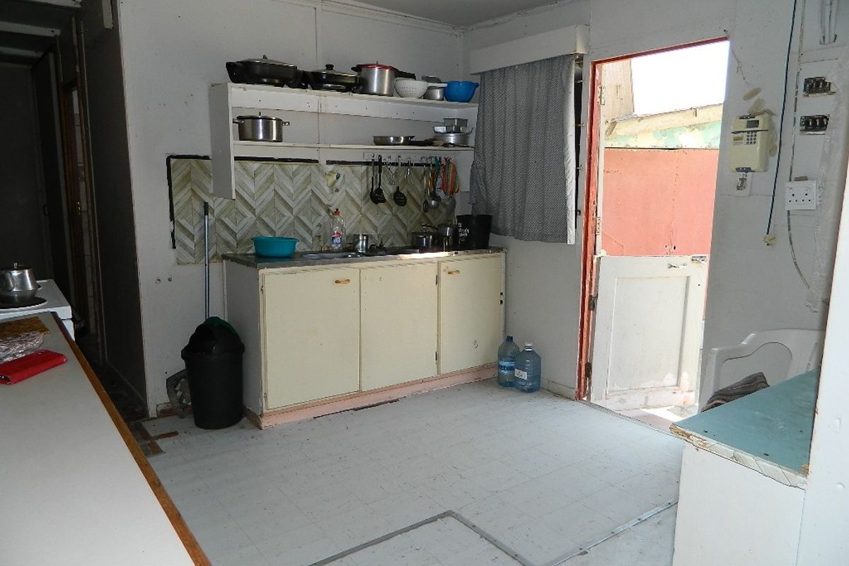 A dated kitchen area featuring basic cabinetry, open shelving, and a tiled backsplash, requiring significant renovation to modernize the space.